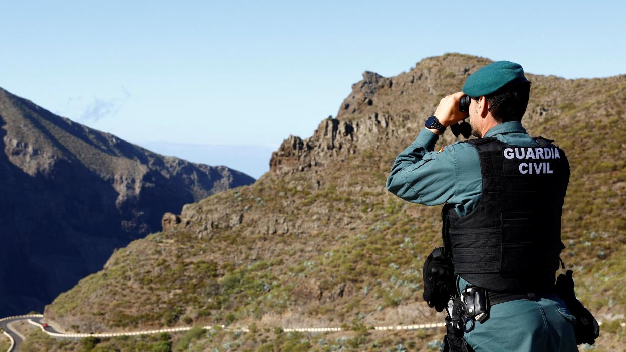 A Guardia Civil officer peering into a ravine with binoculars