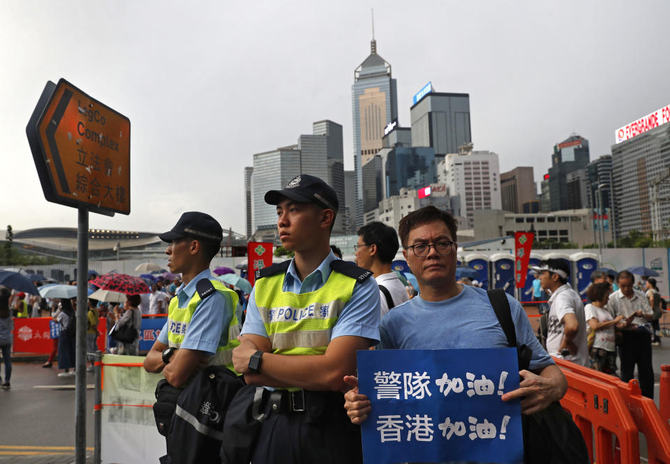 CORRECTS TRANSLATION - A man poses with a picture next to police officers with a placard reads" Go Police ! " during a counter-rally in support of the police in Hong Kong Saturday, July 20, 2019. A counter-rally in support of the police was held Saturday evening. Thousands of people under umbrellas and overcast skies filled a park in central Hong Kong. (AP Photo/Vincent Yu)