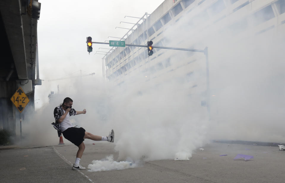 A protester kicks back a tear gas canister during a demonstration next to the city of Miami Police Department, Saturday, May 30, 2020, downtown in Miami. Protests were held throughout the country over the death of George Floyd, a black man who died after being restrained by Minneapolis police officers on May 25.(AP Photo/Wilfredo Lee)