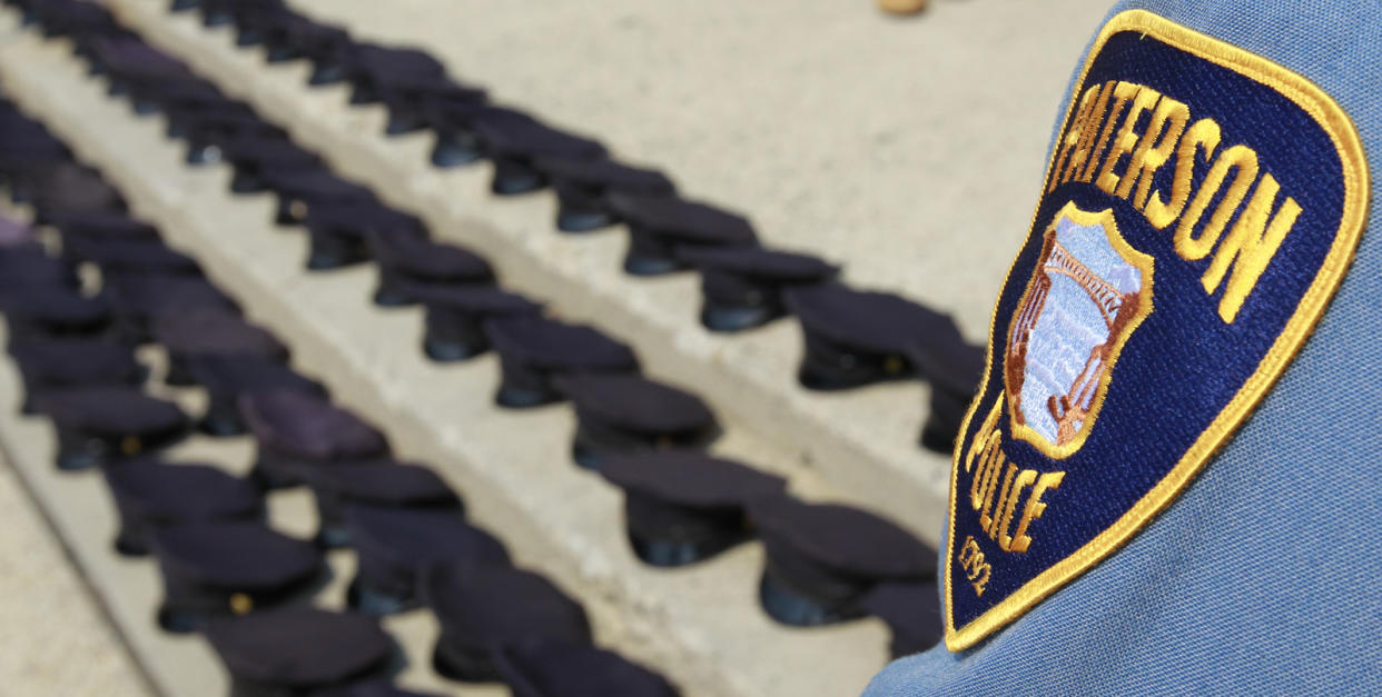 The badge of an active Paterson Police Department officer is seen as police hats are arranged in a line outside of the public safety complex building during a protest by laid-off officers