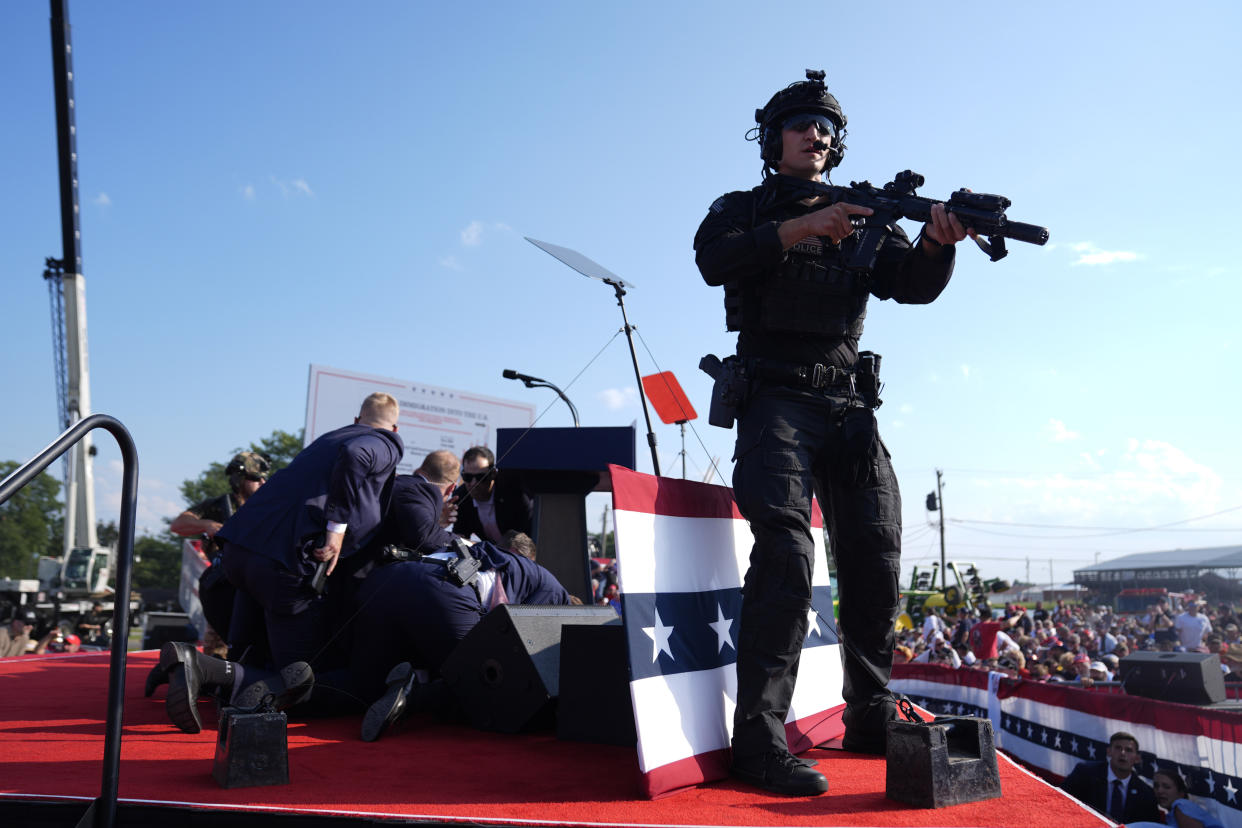 Trump is covered by Secret Service agents, with a heavily armed agent standing on guard, after gunfire at this campaign rally.