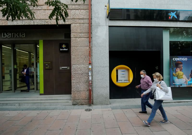 People walk past branches of Bankia and Caixabank in Madrid