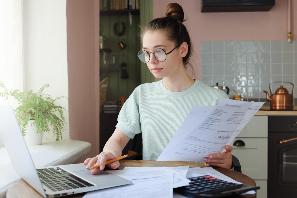 A young woman managing her budget, sitting at a kitchen table with a laptop