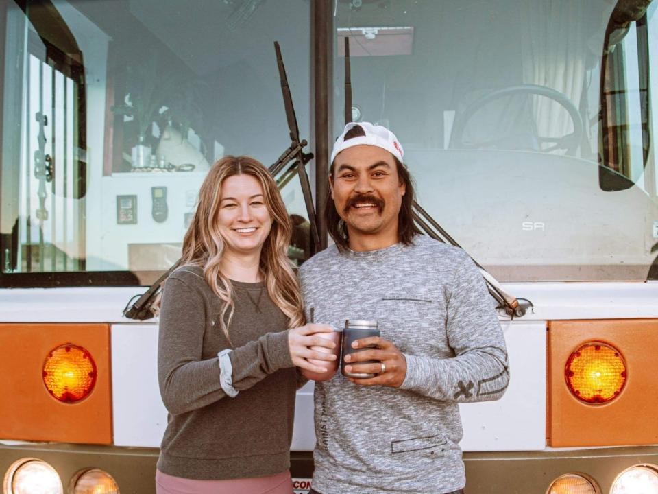 The writer and her partner standing outside their renovated orange school bus