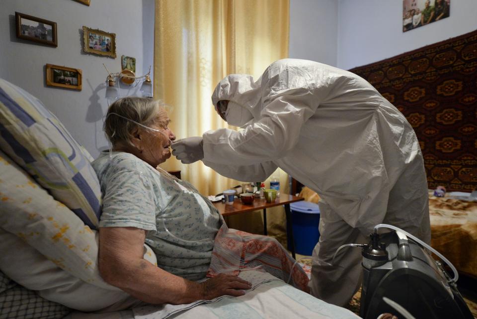 A volunteer in a protective suit and gloves sets an oxygen concentrator to help a suspected coronavirus patient breathe at her apartment in Bishkek, Kyrgyzstan, Friday, July 24, 2020. Volunteers have played a big role in dealing with a wave of coronavirus cases in Kyrgyzstan. Many started doing house calls to patients who couldn't get into a hospital, bringing oxygen concentrators with them. (AP Photo/Vladimir Voronin)