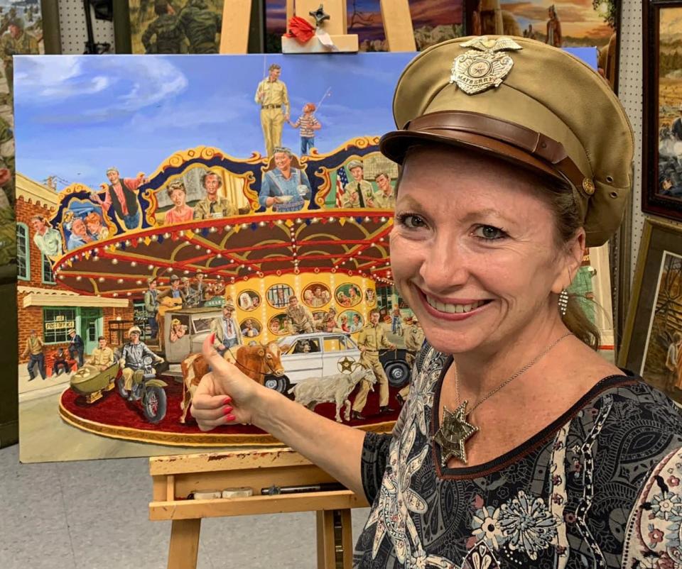 The Social Butterfly Kristi K. Higgins poses for a photo wearing Barney Fife's deputy hat and badge worn by the late Don Knotts in "The Andy Griffith Show." "Mayberry Carousel" painting by Henry E. Kidd.