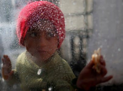 A Palestinian girl looks through a plastic sheet as raindrops are seen, outside her family's house in Al-Shati refugee camp in Gaza City January 17, 2018. REUTERS/Mohammed Salem