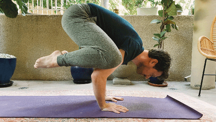 Man practicing an arm balance on a yoga mat