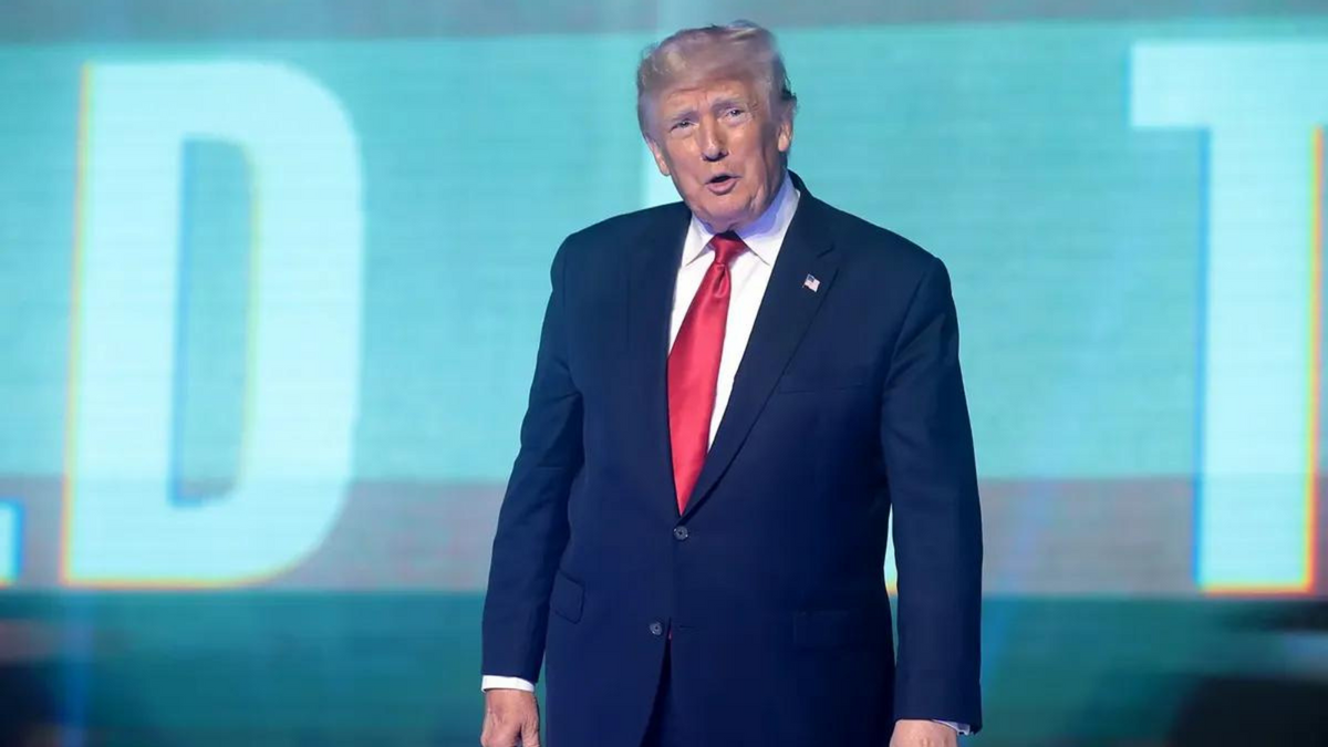 A white man wearing a blue suit stands. 