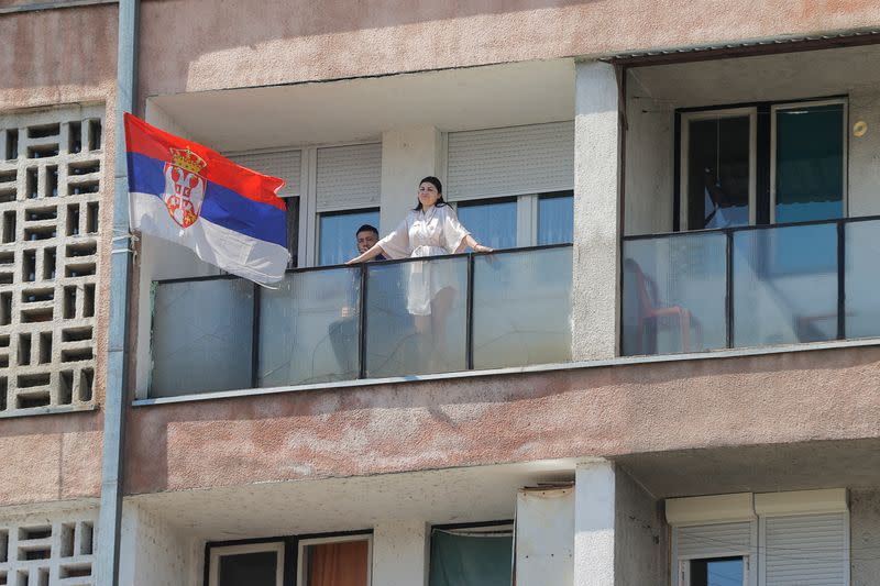 An ethnic Serb couple stand and sit on their balcony in North Mitrovica