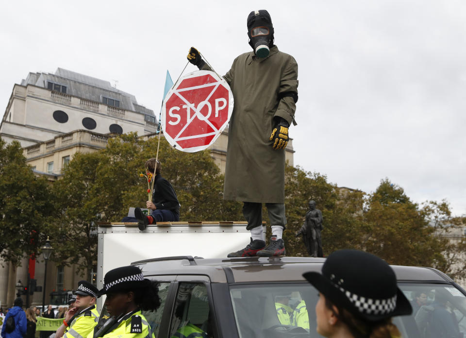 A man wearing a gas mask stand on top of a car as other demonstrators block Trafalgar Square in central London Monday, Oct. 7, 2019. Extinction Rebellion movement blocked major roads in London, Berlin and Amsterdam on Monday at the beginning of what was billed as a wide-ranging series of protests demanding new climate policies. (AP Photo/Alastair Grant)