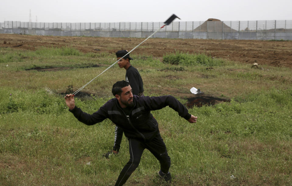 A protester hurls stones near the fence of the Gaza Strip border with Israel, marking first anniversary of Gaza border protests east of Gaza City, Saturday, March 30, 2019. Tens of thousands of Palestinians gathered Saturday at rallying points near the Israeli border to mark the first anniversary of weekly protests in the Gaza Strip, as Israeli troops fired tear gas and opened fire at small crowds of activists who approached the border fence. (AP Photo/Adel Hana)