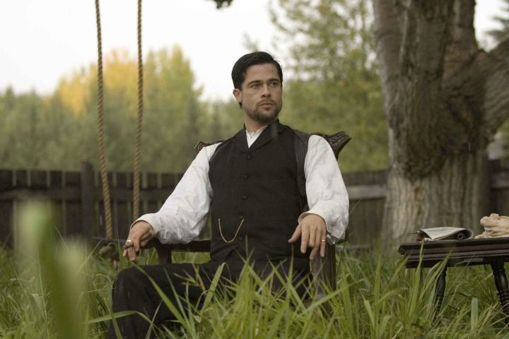 Brad Pitt as Jesse James sitting in a chair.