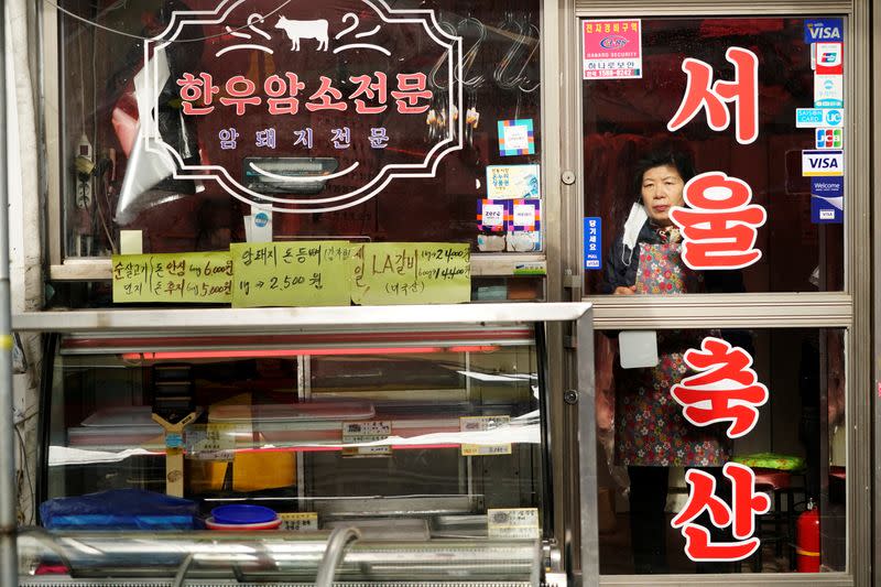 A woman looks on employees from a disinfection service company sanitizing a traditional market in Seoul