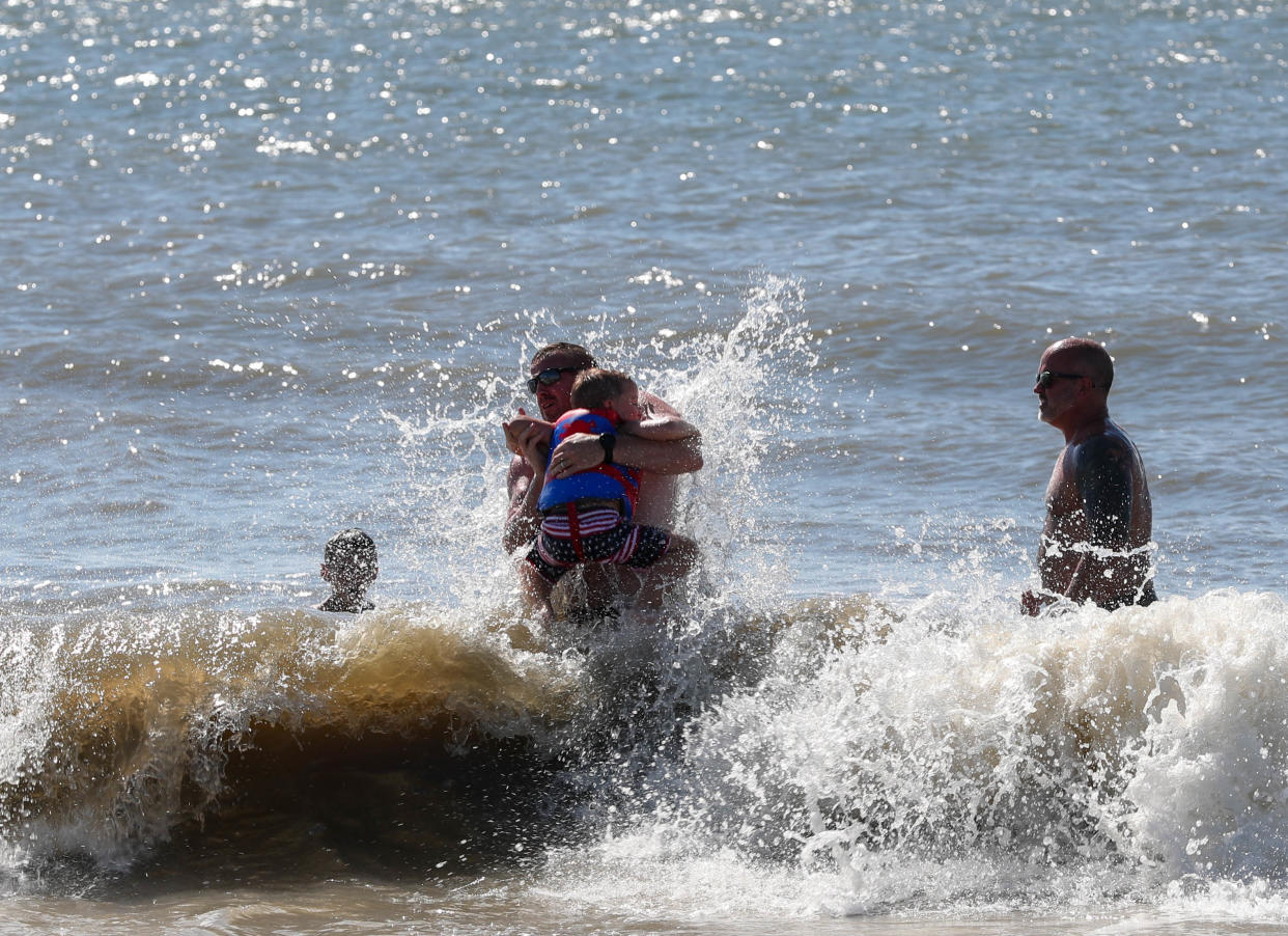 A beachgoer lifts up a child as a wave crashes on them on Thursday, August 8, 2024 as Tropical Storm Debby continued to churn up the ocean.