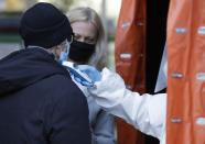 A medical worker takes a man's temperature at a COVID-19 testing center in Warsaw, Poland, Thursday, Oct. 22, 2020. With cases surging in central Europe, some countries are calling in soldiers, firefighters, students and retired doctors to help shore up buckling health care systems. Many faced a shortage of medical personnel even before the pandemic, and now the virus has sickened many health workers, compounding the shortfall. (AP Photo/Czarek Sokolowski)