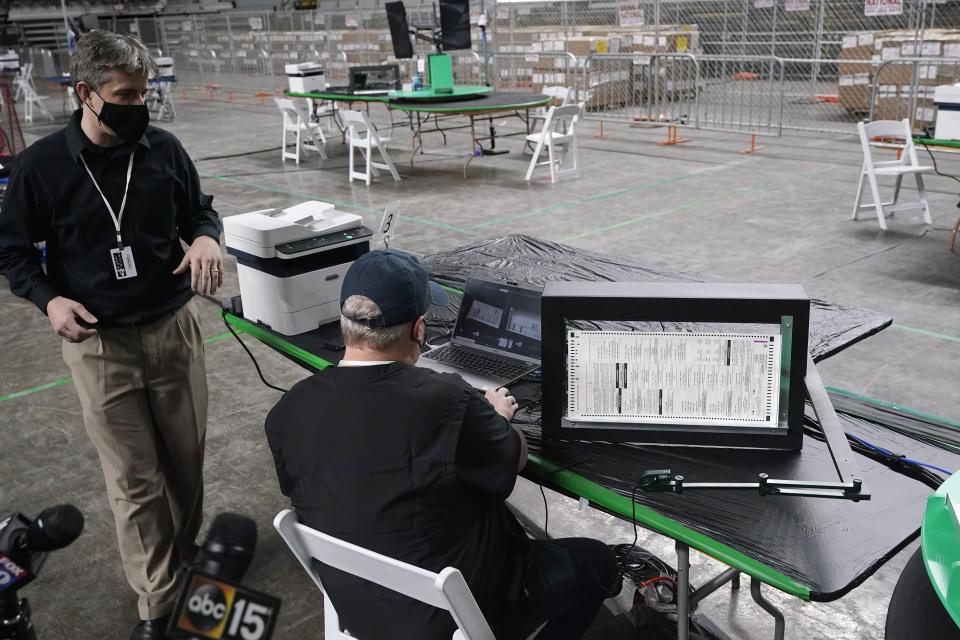 Cyber Ninjas owner Doug Logan, left, a Florida-based consultancy, talks about overseeing a 2020 election ballot audit ordered by the Republican lead Arizona Senate at the Arizona Veterans Memorial Coliseum, as a Cyber Ninjas IT technician demonstrates a ballot scan during a news conference Thursday, April 22, 2021, in Phoenix. The equipment used in the November election won by President Joe Biden and the 2.1 million ballots were moved to the site Thursday so Republicans in the state Senate who have expressed uncertainty that Biden's victory was legitimate can recount them and audit the results. (AP Photo/Ross D. Franklin)