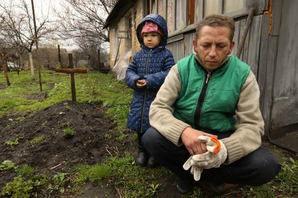 A 4-year-old girl and her father next to a grave with a simple wooden cross