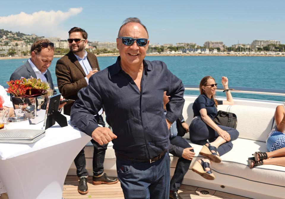 A man poses on a boat as people lounge behind him.