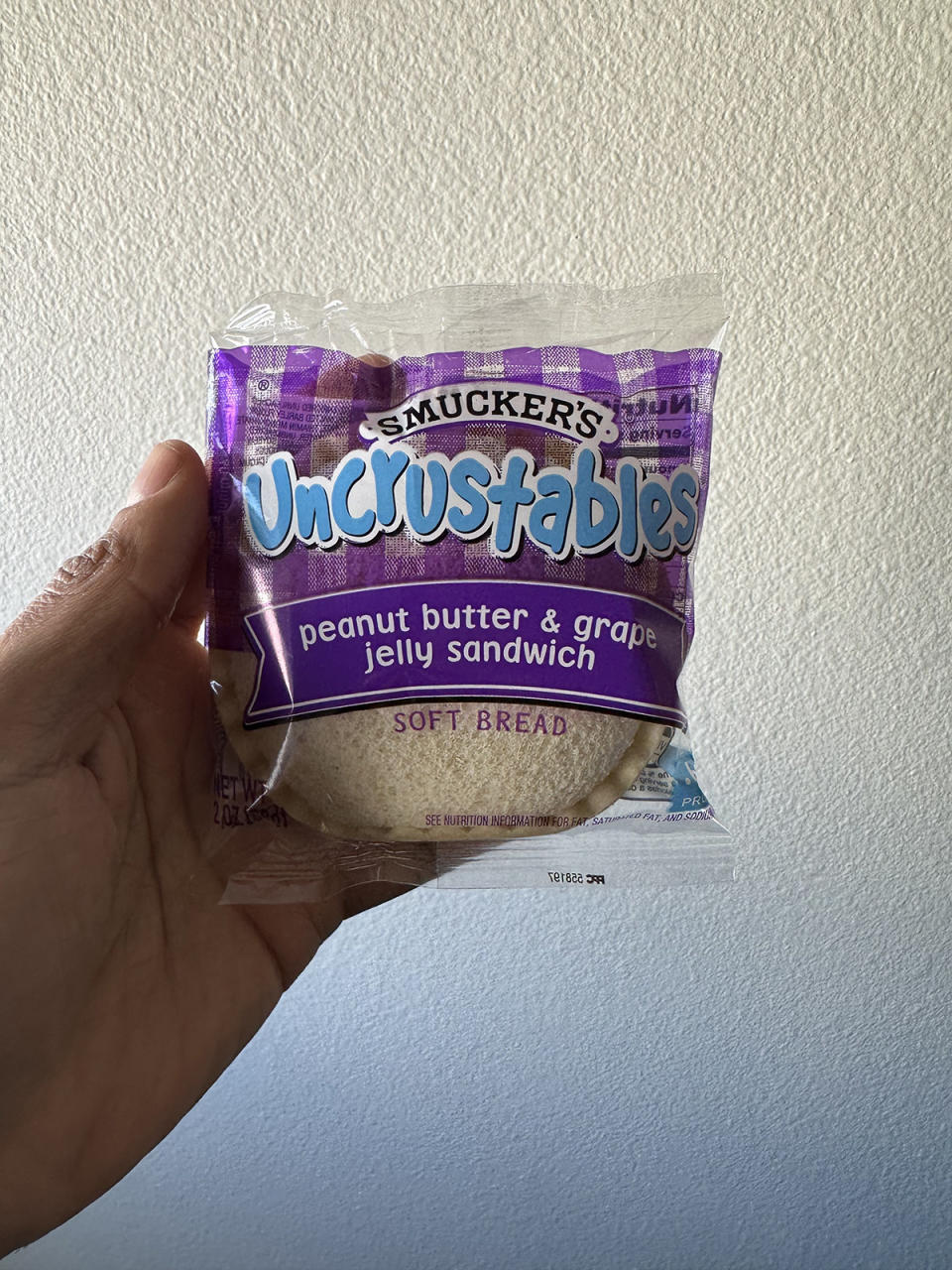 A hand holding a Smucker's Uncrustables Peanut Butter & Grape Jelly Sandwich bag