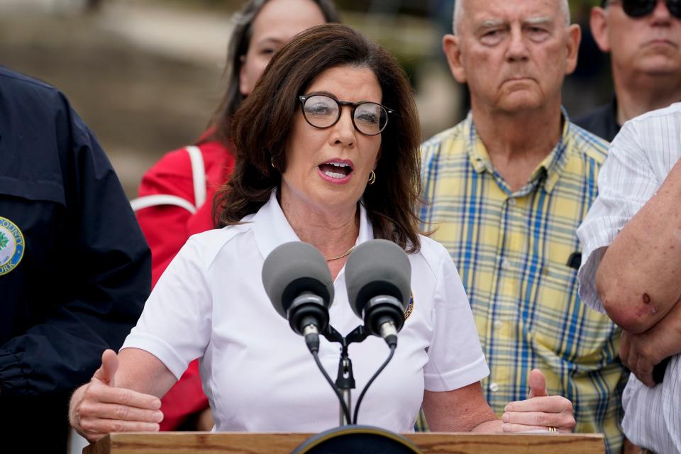 Governor Kathy Hochul, alongside an entourage of emergency workers and officials, speaks to members of the media on the floodwater-damaged Main Street, Monday, July 10, 2023, in Highland Falls, N.Y. Heavy rain has washed out roads and forced evacuations in the Northeast as more downpours were forecast throughout the day. One person in New York's Hudson Valley has drowned as she was trying to leave her home. (AP Photo/John Minchillo)