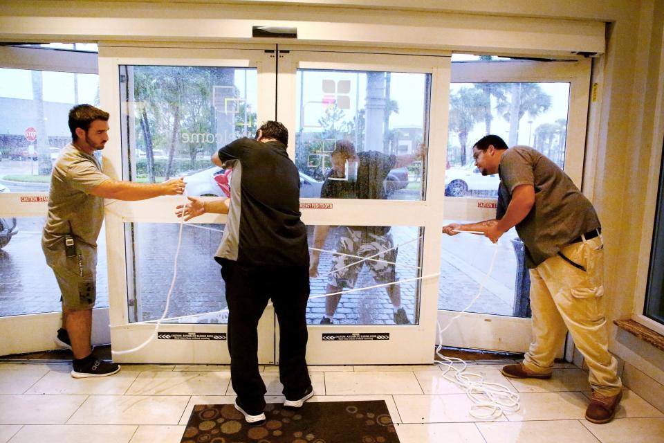 Hilton employees Louie Fonseca, Frankie Monica, Bryan Kinbacher and Jaime Miranda use rope to secure the front door at the Hilton Garden Inn in Fort Myers (AP)