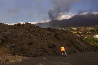 A scientist with the Canary Islands' volcanology institute, Involcan, collects a rock of lava during field work in the surroundings of the volcano on the Canary island of La Palma, Spain, Saturday, Oct. 30, 2021. Scientists from around the world flocking to an eastern Atlantic Ocean island are using an array of new technologies available to them in 2021 to scrutinize — from land, sea, air, and even space — a rare volcanic eruption. But despite technological and scientific leaps, predicting volcanic eruptions and, more crucially, how they end, remains a mystery. (AP Photo/Emilio Morenatti)