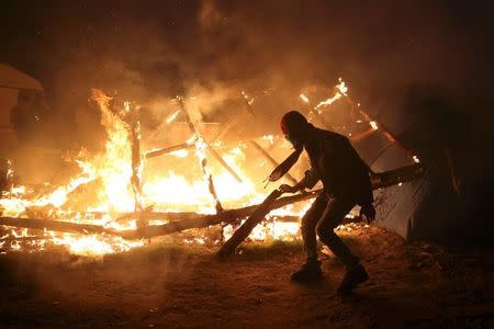 A migrant is seen in silhouette near flames from a burning makeshift shelter on the second day of the evacuation of migrants and their transfer to reception centers in France, as part of the dismantlement of the camp called the "Jungle" in Calais, France, October 25, 2016. REUTERS/Neil Hall TPX IMAGES OF THE DAY