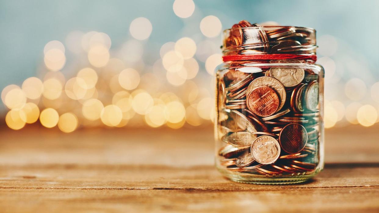 donation money jar filled with coins in front of holiday lights