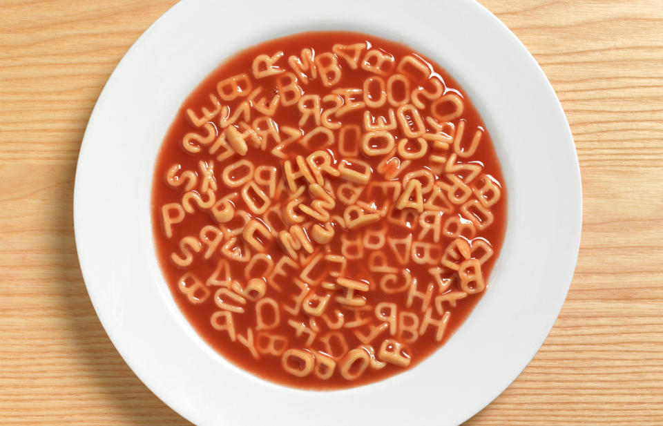 alphabet soup in a white bowl on a beige wooden table