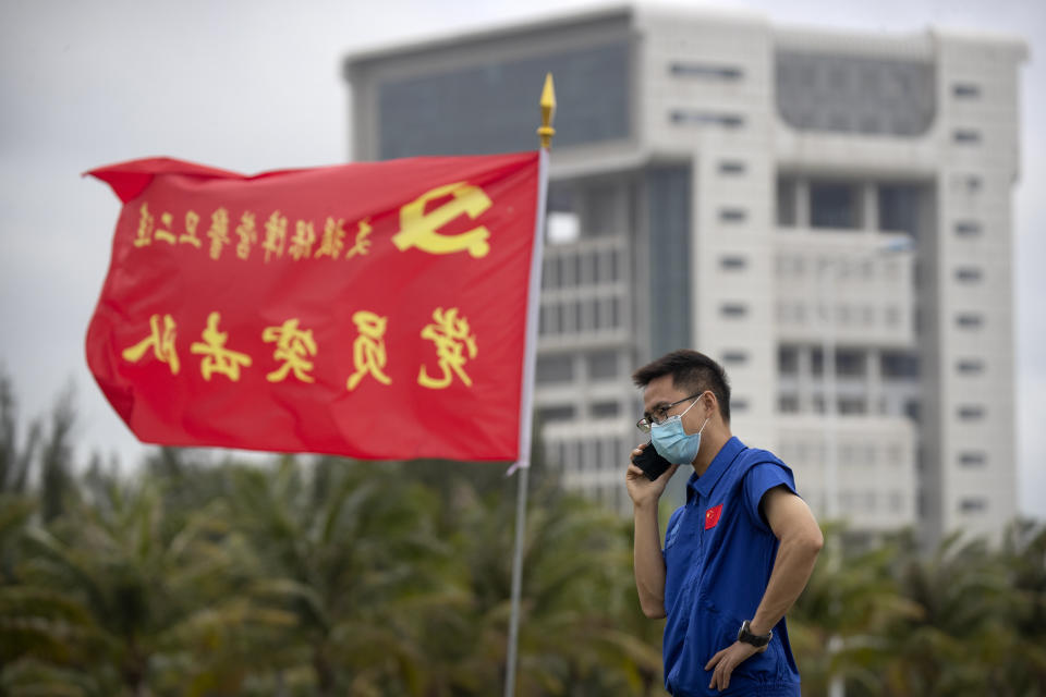 A worker talks on a cellphone near a flag with the logo of the Communist Party of China at the Wenchang Space Launch Site in Wenchang in southern China's Hainan province, Monday, Nov. 23, 2020. Chinese technicians were making final preparations Monday for a mission to bring back material from the moon's surface for the first time in nearly half a century — an undertaking that could boost human understanding of the moon and of the solar system more generally. (AP Photo/Mark Schiefelbein)