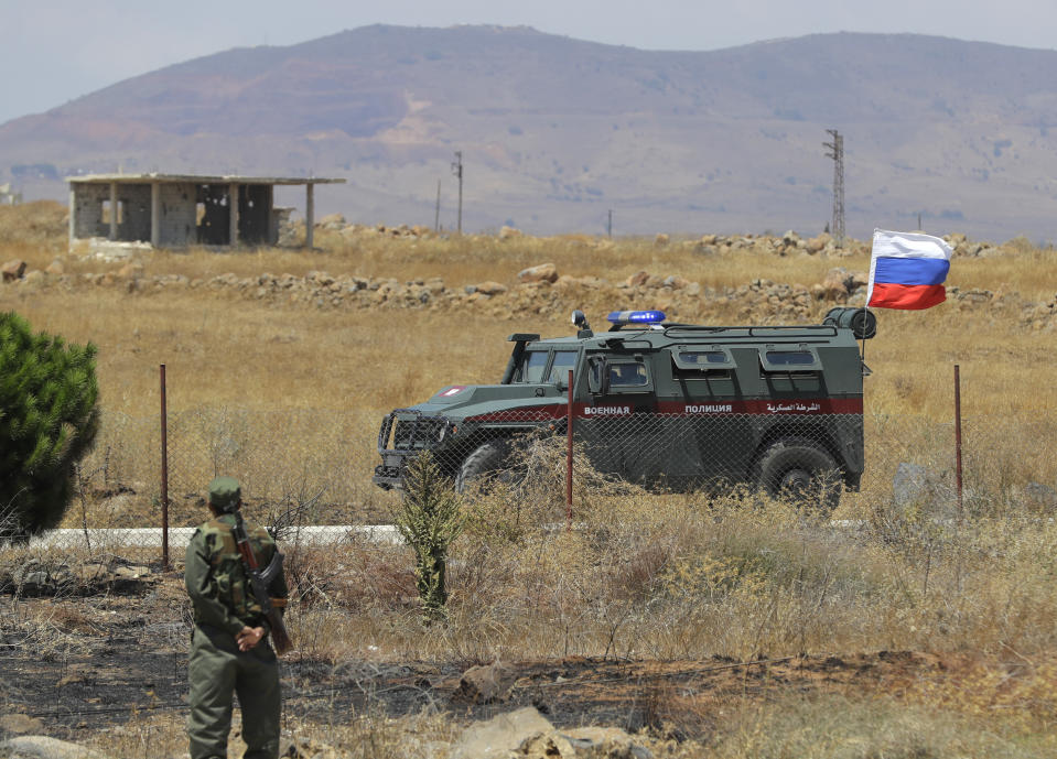 Syrian army soldier stands guard as Russian military police vehicle passes by near the town of Alhureyeh, Syria, Tuesday, Aug. 14, 2018. The Russian military said Tuesday that its forces in Syria will help U.N. peacekeepers fully restore patrols along the frontier with the Israeli-occupied Golan Heights, reflecting Moscow's deepening role in mediating between the decades-old foes. (AP Photo/Sergei Grits)