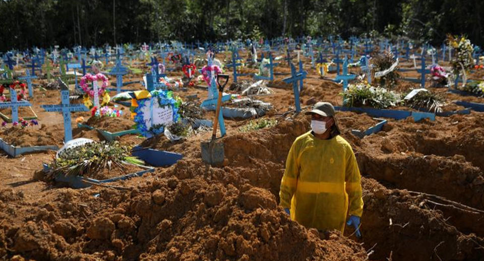 Grave digger prepares another grave with hundreds of crosses in the background.