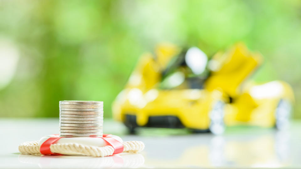 A conceptual image for car insurance that shows stacked coins with a blurred supercar in the background. 