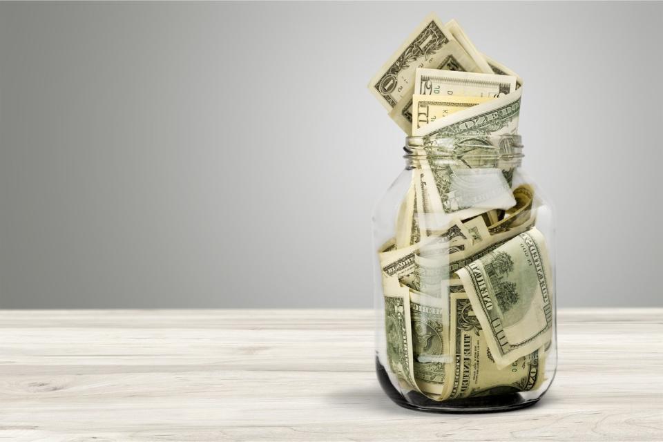 A jar full of bills in various denominations sitting on a wooden table.