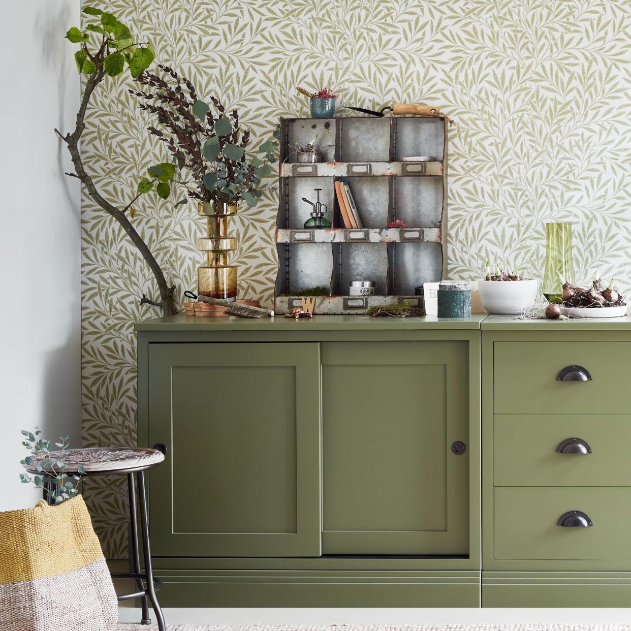  An olive green cabinet with a wallpaper backdrop. 