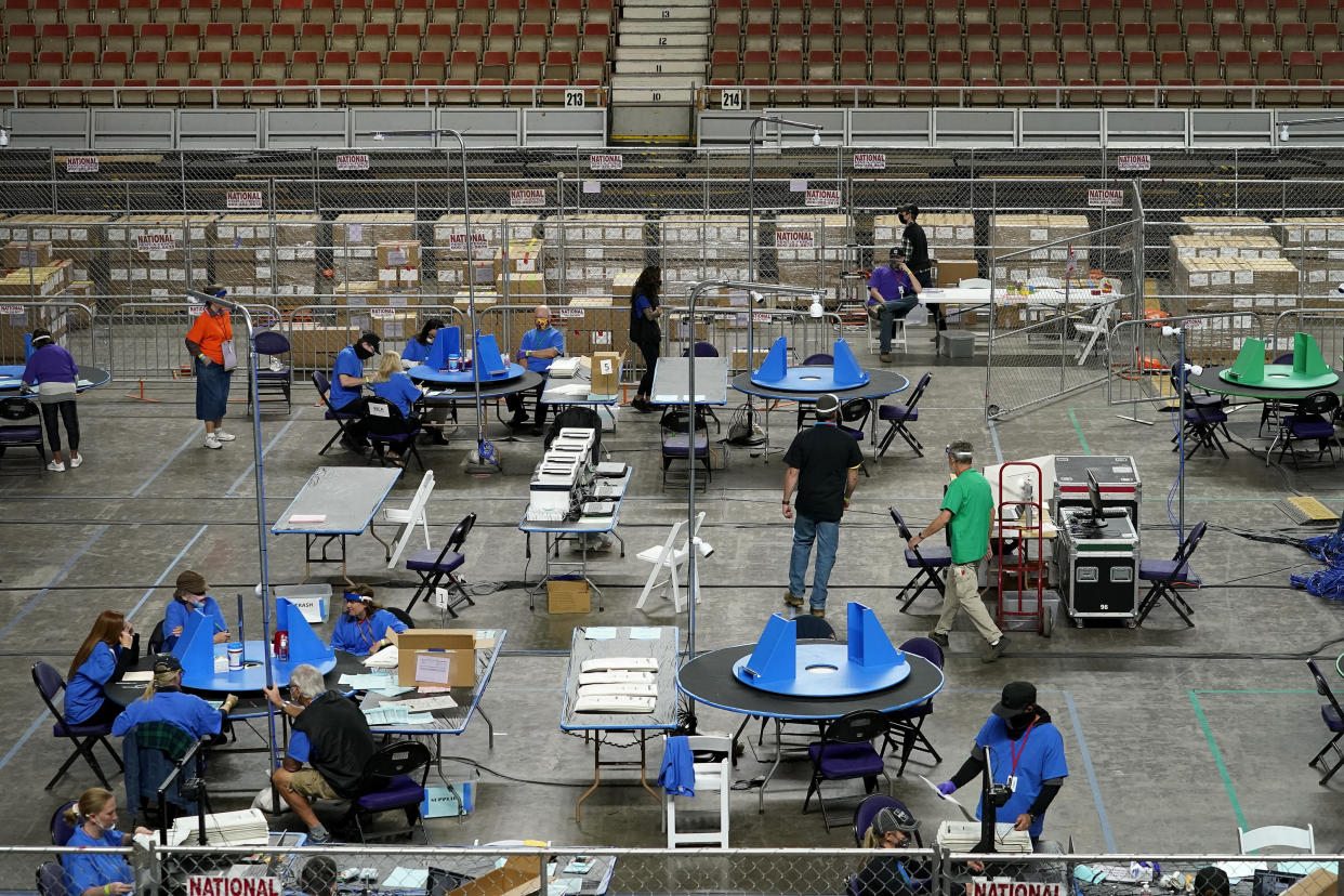 About a dozen contractors, many wearing royal blue T-shirts and sitting at round folding tables counting, with cardboard boxes stacked behind them.