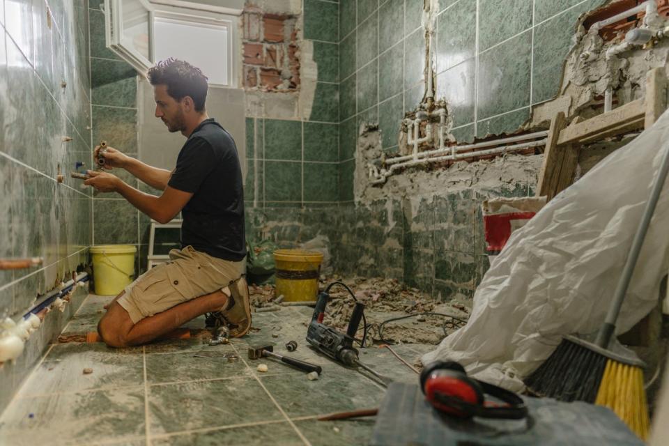 A man installs tiles on the walls of a bathroom undergoing a remodel.