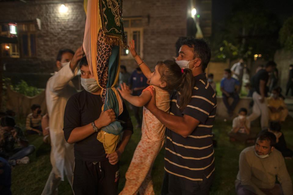 A Kashmiri Shiite Muslim helps her daughter to touch the religious flag at of the ceremony commemorating Muharram inside the lawn of a residential house in Srinagar Indian-controlled Kashmir, Friday, Aug. 21, 2020. Observing the Muslim month of Muharram, which marks the martyrdom of the Prophet Muhammad’s grandson in the battle of Karbala, is an article of faith. But as the coronavirus spreads in Indian-controlled Kashmir, Shiite Muslims prefer to commemorate the holy days inside their home following the advice of religious scholars and health experts in the disputed region’s main city. (AP Photo/ Dar Yasin)