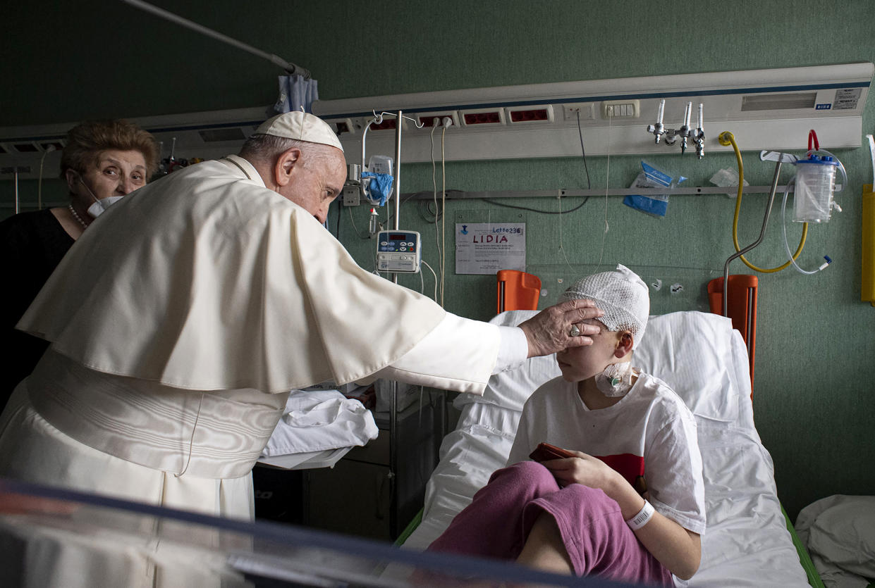 Pope Francis places his hand on the forehead of a child in a hospital.