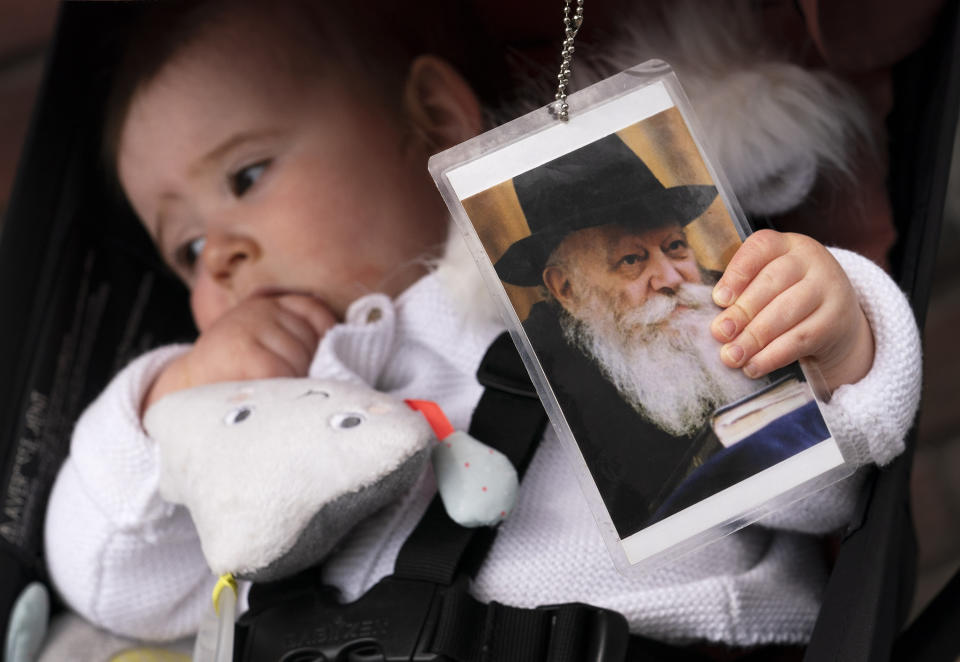 FILE - A girl clutches a photo of the late Rabbi Menachem Schneerson during a holiday celebration of Lag BaOmer in front of the Chabad Lubavitch World Headquarters, Friday, April 30, 2021 in New York. The Lag BaOmer holiday is one of the happiest days on the calendar for the ultra-Orthodox Jewish community — a time of mass celebrations in honor of a revered sage. (AP Photo/Mark Lennihan, File)