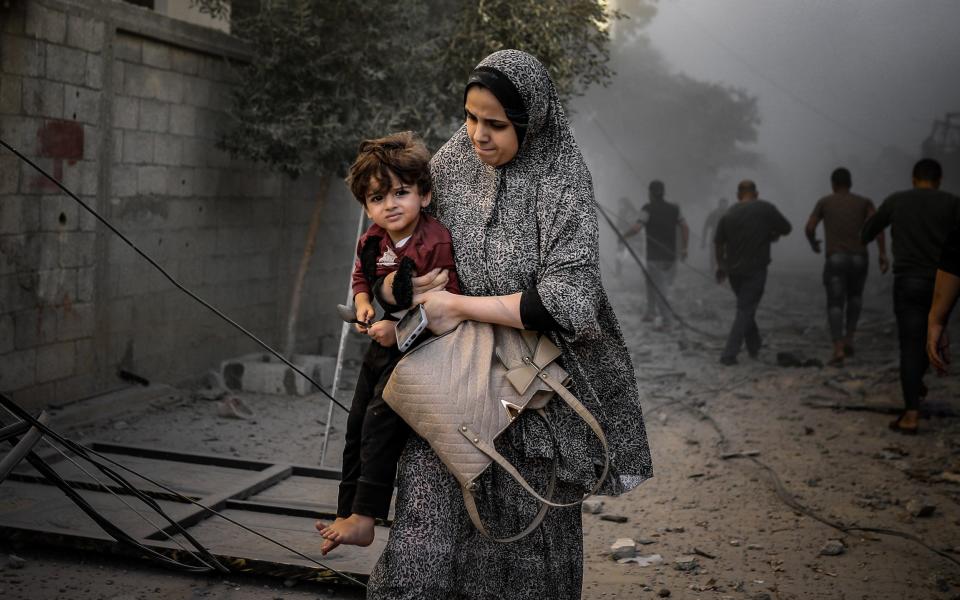 A Palestinian woman walks with her child among rubbles of buildings destroyed after Israeli attacks on Al-Maghazi refugee camp