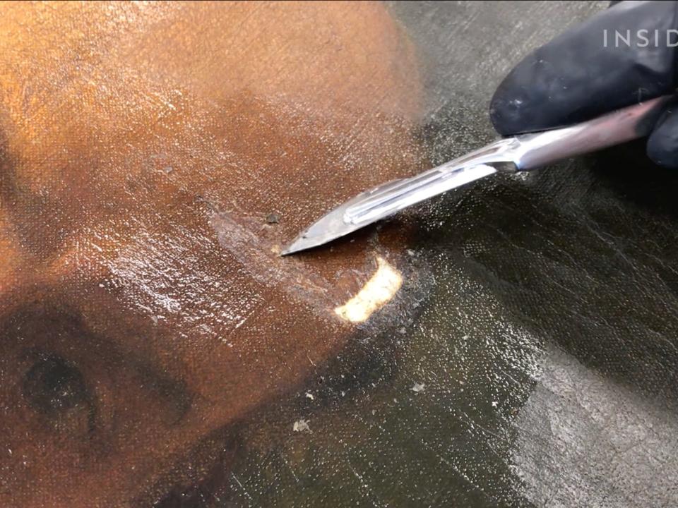 A conservator uses a knife to remove paper from canvas.