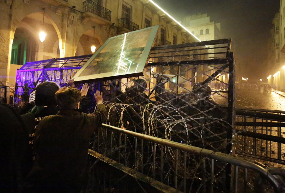 Anti-government protesters throw a glass panel against the riot police who are standing behind barriers defense, during ongoing protests against the political elites who have ruled the country for decades, in Beirut, Lebanon, Sunday, Jan. 19, 2020. Lebanese security forces used tear gas, water cannons and rubber bullets in clashes with hundreds of anti-government protesters outside the country's Parliament on Sunday, as violence continued to escalate in a week of rioting in the capital. (AP Photo/Hassan Ammar)