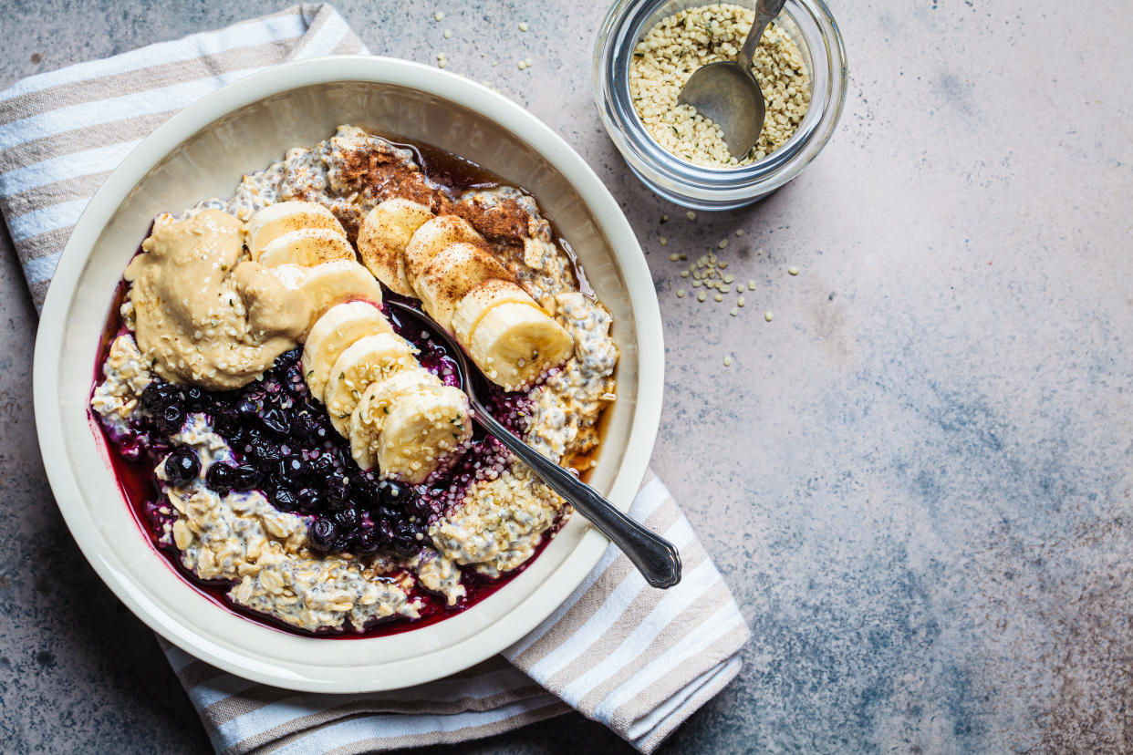 Winter breakfast concept. Overnight oatmeal with banana, berry, chia seeds, sesame tahini, cinnamon and syrup in bowl, top view, dark background.