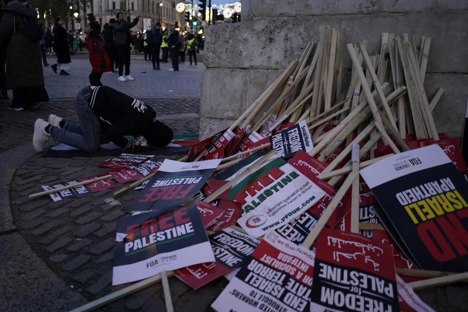 A protester pays next to a pile of discarded placards during a pro-Palestinian demonstration in Trafalgar Square in London, Saturday, Nov. 25, 2023. (AP Photo/Alberto Pezzali)