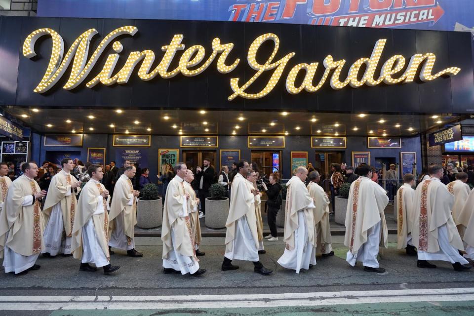 Priests walk past a Winter Garden sign.