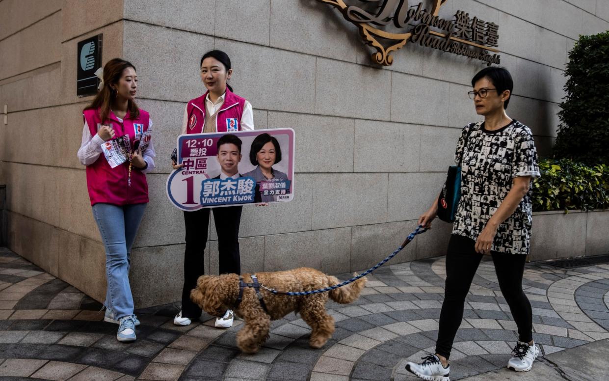 Two women hold a sign for a candidate near a polling station for district elections in Hong Kong on December 10, 2023