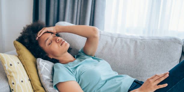 sick young woman lying on the couch and holding her head with hand ill woman lying on the sofa with high temperature