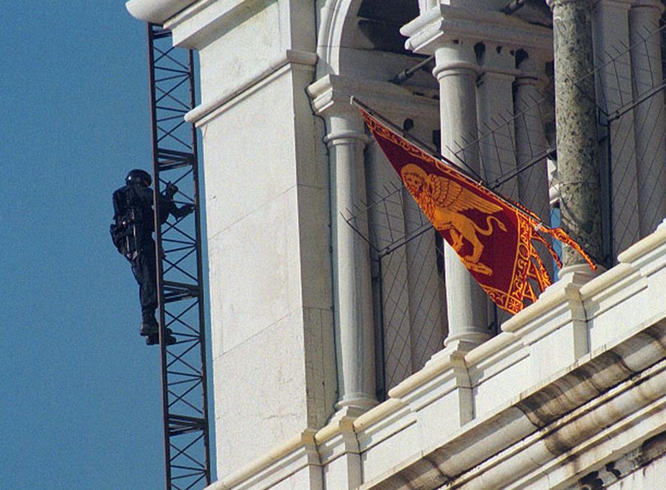 FILE - In this Friday May 9, 1997 file photo, a policeman of the Italian special forces climbs past the flag of self-proclaimed Venetian separatists who had occupied the bell tower in St. Mark's square, in Venice, Italy. Italian special operations units on Wednesday, April 2, 2014, arrested 24 secessionists who were allegedly planning a violent campaign aimed at making the wealthy northeastern Veneto region independent. Police said in a statement that the group had built an armored vehicle that they intended to deploy in St. Mark's Square in Venice — reminiscent of a 7 ½-hour takeover of the piazza's famed bell tower by secessionists in 1997. TV footage showed the so-called tank was a tractor that had been armed in some fashion. Italian media reported that the secessionists intended to deploy the vehicle on the eve of European Parliamentary elections in May, which will be a measure of growing anti-Europe sentiment arising from harsh austerity measures to fight the economic crisis. (AP Photo/Franco Proietti, File)